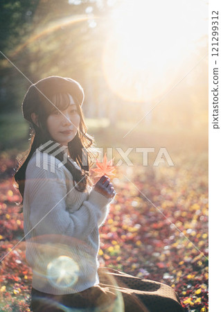 A young woman wearing a beret looking at autumn leaves 121299312