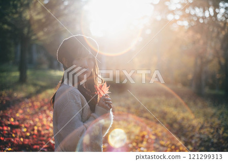 A young woman wearing a beret looking at autumn leaves 121299313