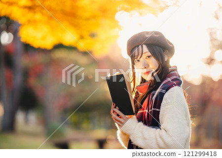 Autumn reading: A young woman reading in a park with autumn leaves 121299418