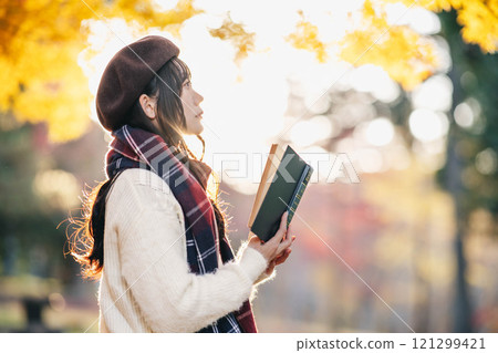 Autumn reading: A young woman reading in a park with autumn leaves 121299421