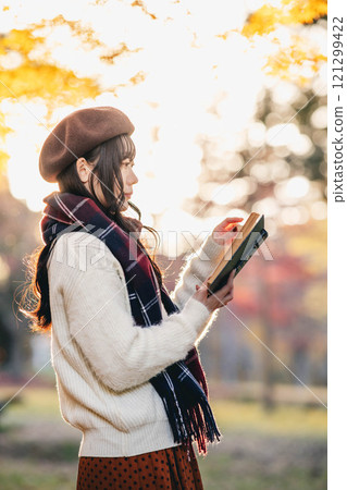 Autumn reading: A young woman reading in a park with autumn leaves 121299422