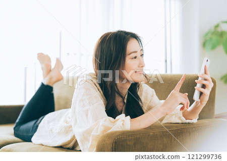 一個女人躺在沙發上，看著她的智能手機 121299736