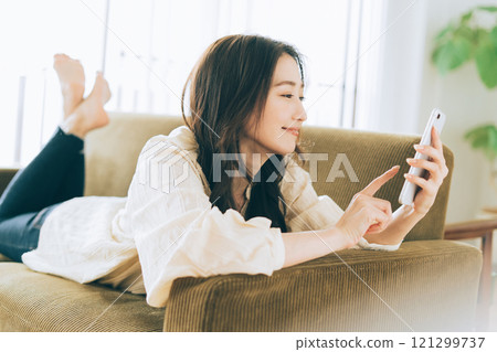 A woman lying on the sofa and looking at her smartphone 121299737