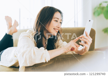 A woman lying on the sofa and looking at her smartphone 121299740