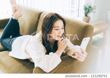 一個女人躺在沙發上，看著她的智能手機 121299741