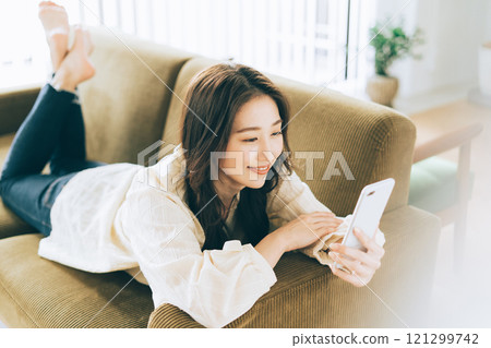 A woman lying on the sofa and looking at her smartphone 121299742