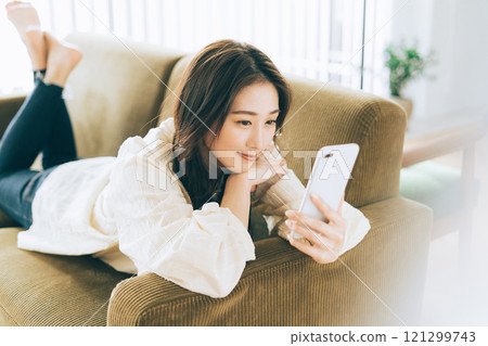 A woman lying on the sofa and looking at her smartphone A woman lying on the sofa and looking at her smartphone 121299743