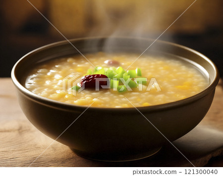A steaming bowl of millet and pumpkin porridge on a wooden table 121300040