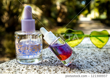 Tropical summer cosmetics. Cosmetic serum, oil extracts against lush greenery of tropics. Skin care products. Beauty nature. Heart-shaped sunglasses. 121300937
