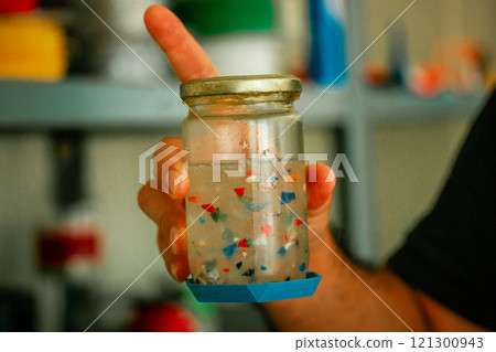 Colorful plastic parts floating inside of a bottle in a hand. Separating plastic by type in a laboratory. Zero waste laboratory. Separation process.  121300943