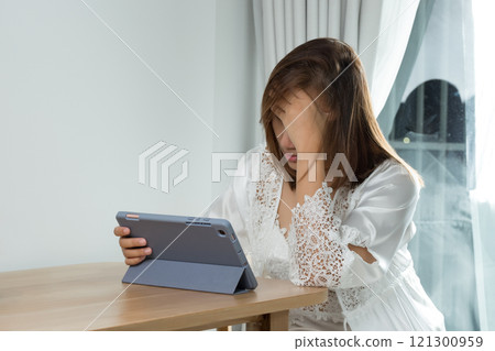 A woman experiences eye strain and fatigue while reading her work schedule on a tablet at night. 121300959