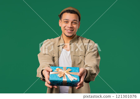 Stylish Excited Man Holding Gift Box And Gives It By Hands To Camera on green. 121301076
