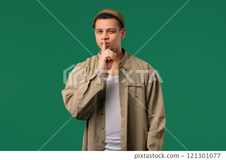 Handsome man with gesture of shh, secret, silence, conspiracy, gossip on green Handsome man with gesture of shh, secret, silence, conspiracy, gossip on green 121301077