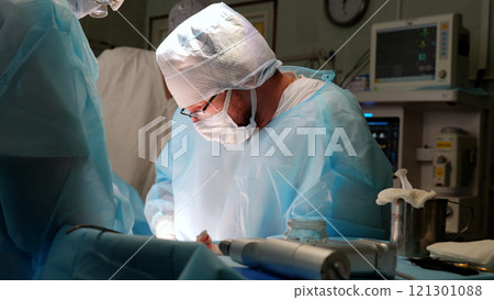 Focused surgeon in blue scrubs performs a precise medical procedure in a busy hospital operating room, highlighting teamwork and professionalism in healthcare Focused surgeon in blue scrubs performs a precise medical procedure in a busy hospital operating room, highlighting teamwork and professionalism in healthcare 121301088
