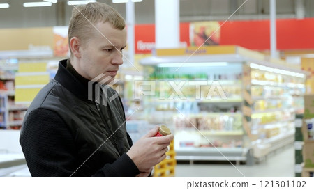 Man makes mindful selections at the supermarket, evaluating labels and comparing products to support his wellness. A customer in black studies the label on a bottle of sauce Man makes mindful selections at the supermarket, evaluating labels and comparing products to support his wellness. A customer in black studies the label on a bottle of sauce 121301102