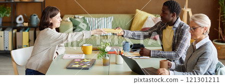 Website header shot of young man of African American ethnicity passing female colleague book sitting at table during work meeting in office, copy space 121301211