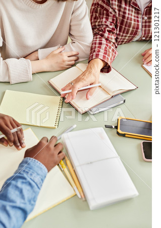 Vertical cropped shot of business team discussing project details at meeting table cluttered with notebooks and office stationery at workplace 121301217