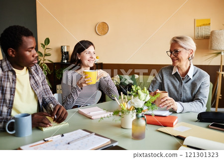 Medium shot of multigenerational team of positive employees and mature female boss networking over cup of coffee during break in office, copy space Medium shot of multigenerational team of positive employees and mature female boss networking over cup of coffee during break in office, copy space 121301323