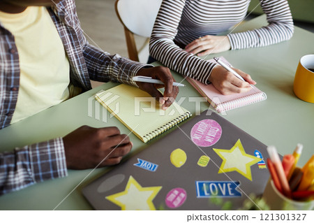 Cropped shot of diverse team of colleagues writing business report in colorful notebooks collaborating at working desk in office 121301327