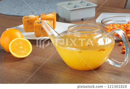 Tea made from frozen briquettes of sea buckthorn, orange and spices in teapot in kitchen. Healthy eating and seasons. Quick beverages to make. 121301828