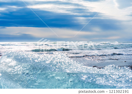 Wave crashing on black sand beach with iceberg breaking from glacier in sunny day Wave crashing on black sand beach with iceberg breaking from glacier in sunny day 121302191