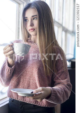 Woman enjoying tea by the window in a bright indoor space. 121302317