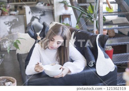 Young woman enjoying cereal while relaxing on a modern sofa. 121302319