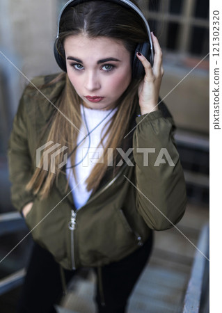 Young woman with headphones, wearing casual fashion, looking focused. 121302320