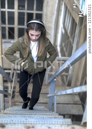 Young woman with headphones, wearing casual fashion, looking focused. 121302321