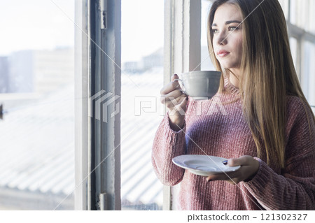 Woman enjoying tea by the window in a bright indoor space. 121302327