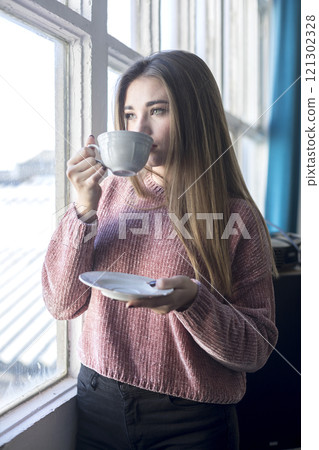 Woman enjoying tea by the window in a bright indoor space. Woman enjoying tea by the window in a bright indoor space. 121302328