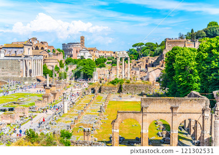 The ancient Roman Forum showcases impressive ruins surrounded by vibrant greenery, with the iconic Colosseum rising majestically in the background under a clear blue sky. The ancient Roman Forum showcases impressive ruins surrounded by vibrant greenery, with the iconic Colosseum rising majestically in the background under a clear blue sky. 121302531