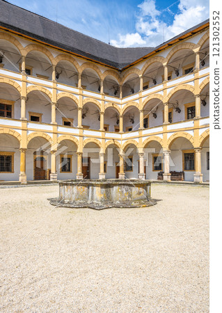 Elegant architecture and historical charm of Velke Losiny Chateau courtyard, featuring arched columns and a central fountain under a bright blue sky in Czechia. 121302552
