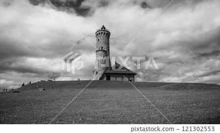 The Dalimil Lookout Tower stands prominently on Vetrov Hill, showcasing its stone structure against a backdrop of dramatic clouds and a grassy landscape, inviting visitors to explore the area. 121302553