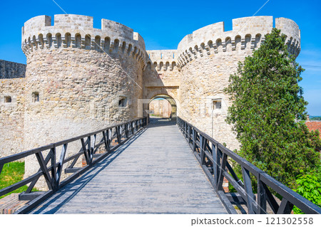 The historic Zindan Gate at Belgrade Fortress stands majestically, flanked by stone towers. A wooden bridge leads visitors into the fortress, surrounded by lush greenery and bright blue skies. The historic Zindan Gate at Belgrade Fortress stands majestically, flanked by stone towers. A wooden bridge leads visitors into the fortress, surrounded by lush greenery and bright blue skies. 121302558