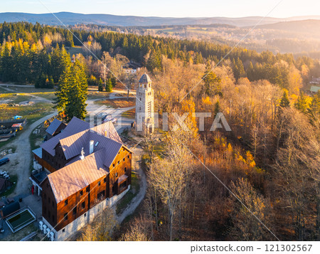 On a sunny autumn morning in the Jizera Mountains, the Bramberk lookout tower and hut stand amidst colorful foliage, inviting visitors to enjoy the breathtaking landscape and peaceful surroundings. On a sunny autumn morning in the Jizera Mountains, the Bramberk lookout tower and hut stand amidst colorful foliage, inviting visitors to enjoy the breathtaking landscape and peaceful surroundings. 121302567