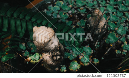 A statue of a woman is surrounded by vibrant green plants 121302787