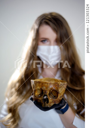 Coronavirus Covid-19 concept. Doctor in rubber gloves holding human skull with mask. 121303324