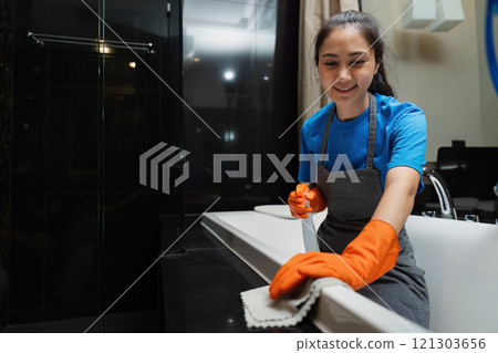 Cleaning online service. yong woman housekeeper cleaning bathtub in bathroom with a cloth. House cleaning service concept Cleaning online service. yong woman housekeeper cleaning bathtub in bathroom with a cloth. House cleaning service concept 121303656