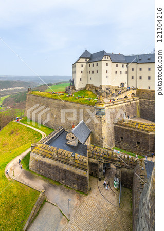 Visitors stroll through the historic Konigstein Fortress, a prominent landmark in Saxony, Germany, showcasing stunning architecture and scenic views of the surrounding landscape. 121304216