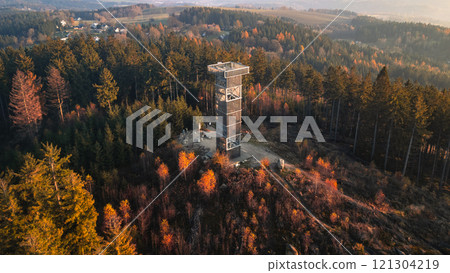 The wooden lookout tower at Cisarsky Kamen near Liberec offers stunning views during an autumn sunset, with colorful foliage and serene forest surroundings creating a peaceful atmosphere. 121304219