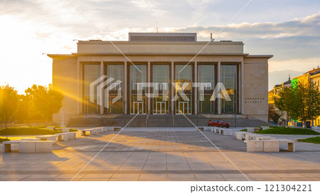 The sun rises, casting golden light on the Janacek Theatre in Brno, highlighting its architectural features and the tranquil atmosphere of the surrounding plaza. 121304221