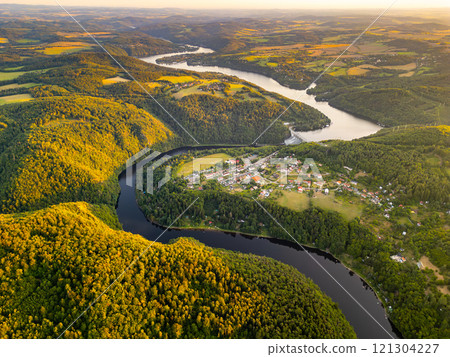 The Slapy Water Reservoir is beautifully illuminated by the evening sun, showcasing its winding paths and lush green hills The Slapy Water Reservoir is beautifully illuminated by the evening sun, showcasing its winding paths and lush green hills 121304227