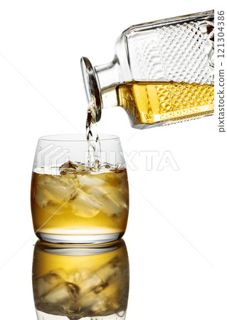 Gold liquor pouring into a glass with ice on a white background. 121304386