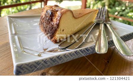 piece of cheesecake on a plate with forks on a wooden tabletop 121304421