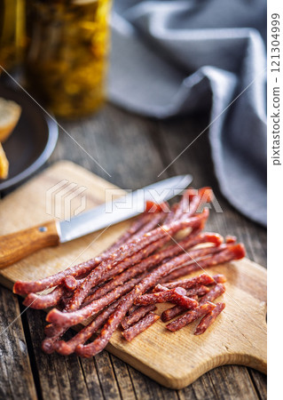 Smoked kabanos. Mini dried thin sausages on cutting board on wooden table. 121304999