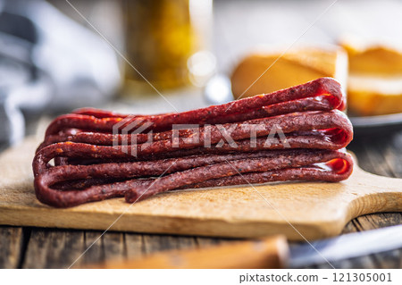 Smoked kabanos. Mini dried thin sausages on cutting board on wooden table. 121305001