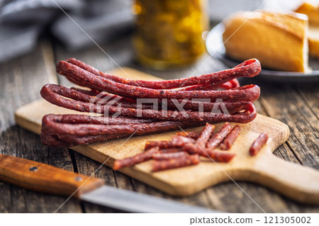 Smoked kabanos. Mini dried thin sausages on cutting board on wooden table. 121305002