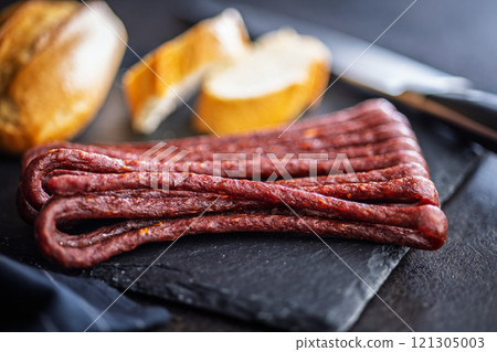 Smoked kabanos. Mini dried thin sausages on cutting board on black table. 121305003