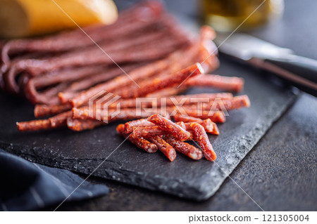 Smoked kabanos. Mini dried thin sausages on cutting board on black table. 121305004